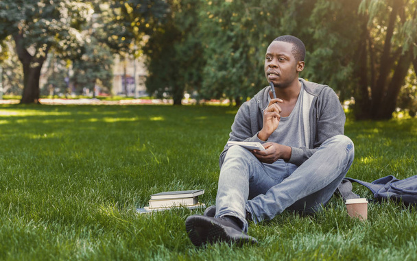 Afrikalı-Amerikalı studen çim üstünde defter ile oturan konsantre - Fotoğraf, Görsel