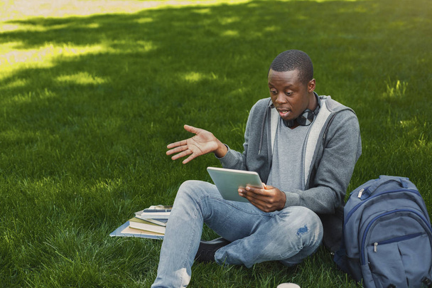 Étonné étudiant afro-américain sur herbe avec tablette à l'extérieur
 - Photo, image