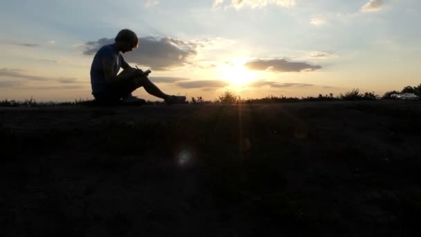 Młody blogger pisze artykuł na trawnik o zachodzie słońca w slo-mo - Materiał filmowy, wideo
