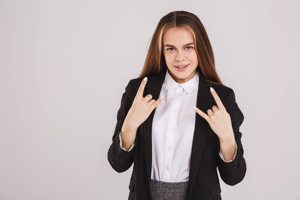 A beautiful young woman showing rock sign on a gray background. Hands gestures concept - Foto, Imagen