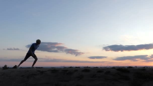 Blond człowiek działa i skacze na trawnik o zachodzie słońca w slo-mo - Materiał filmowy, wideo