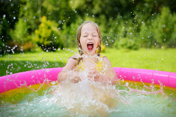 Adorable little girl playing in inflatable baby pool. Happy kid splashing in colorful garden play center on hot summer day. Summer activities for kids. - Photo, Image