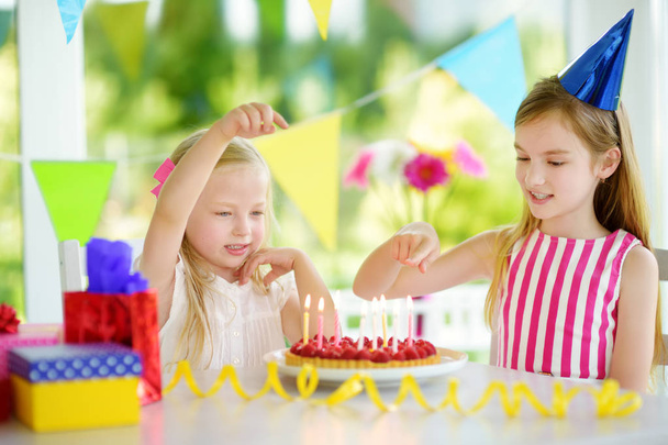 Adorable girl having birthday party at home, blowing candles on birthday cake. Kids birthday party with colorful decorations, gifts and banners. - Foto, immagini