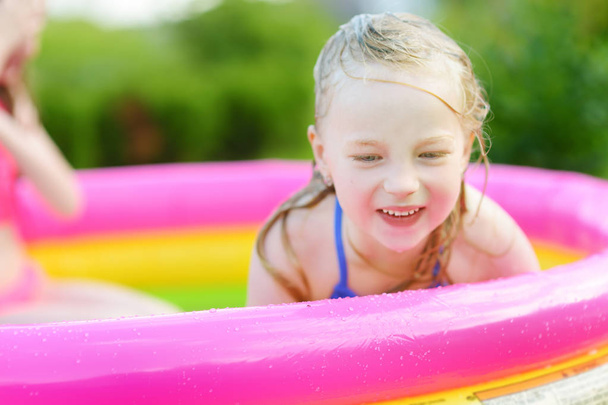 Adorable little girl playing in inflatable baby pool. Happy kid splashing in colorful garden play center on hot summer day. Summer activities for kids. - Фото, зображення