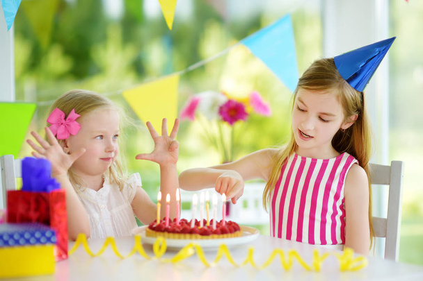 Adorable girl having birthday party at home, blowing candles on birthday cake. Kids birthday party with colorful decorations, gifts and banners. - Photo, image