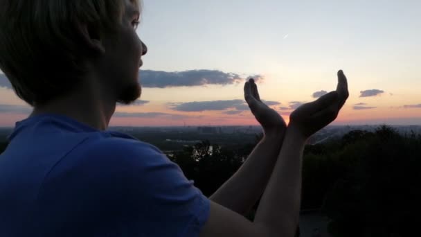 芸術家気取りの男がスローモーションでキエフで夕暮れ時彼の手に太陽を保持します。 - 映像、動画