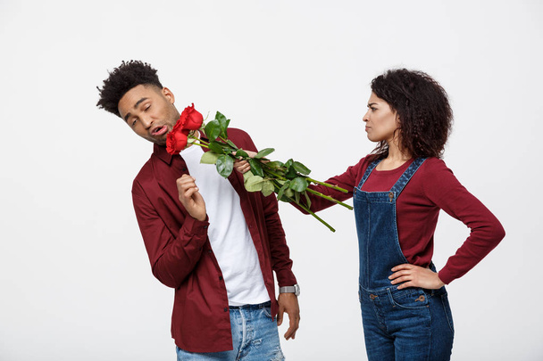 Πορτρέτο μιας απογοητευμένος νεαρής γυναίκας που κατέχουν κόκκινο τριαντάφυλλο με ενώ στέκεται και θυμωμένος με το φίλο που απομονώνονται σε λευκό φόντο - Φωτογραφία, εικόνα