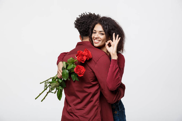 Paarkonzept - junges afrikanisch-amerikanisches Paar umarmt sich und hält romantische rote Rosen in der Hand. - Foto, Bild