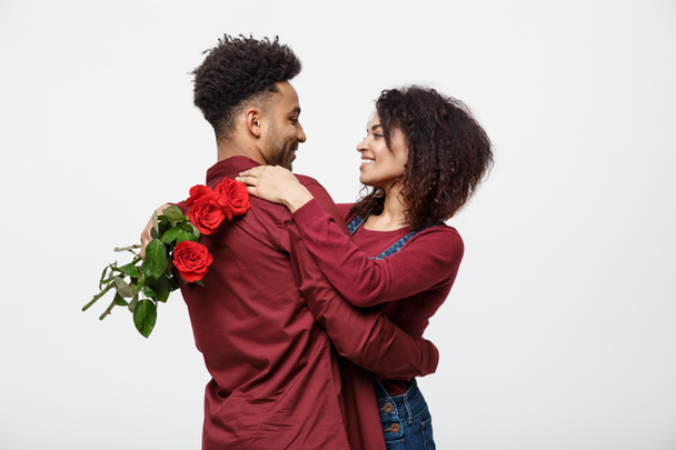 カップルのコンセプト - 若いアフリカ系アメリカ人カップル huging と持株ロマンチックな赤いバラ. - 写真・画像