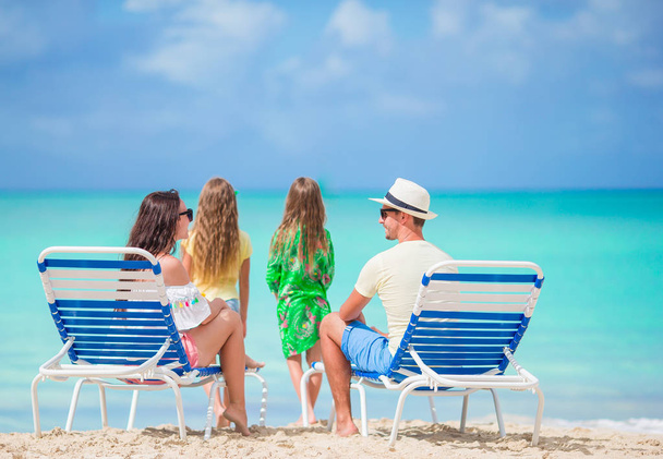 Feliz hermosa familia de cuatro en la playa. Los padres se relajan en la tumbona y los niños se divierten en la costa
 - Foto, imagen
