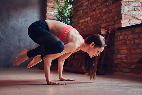 Femme séduisante d'âge moyen équilibrant sur les mains et pratiquant le yoga dans une chambre avec mezzanine intérieure
. - Photo, image