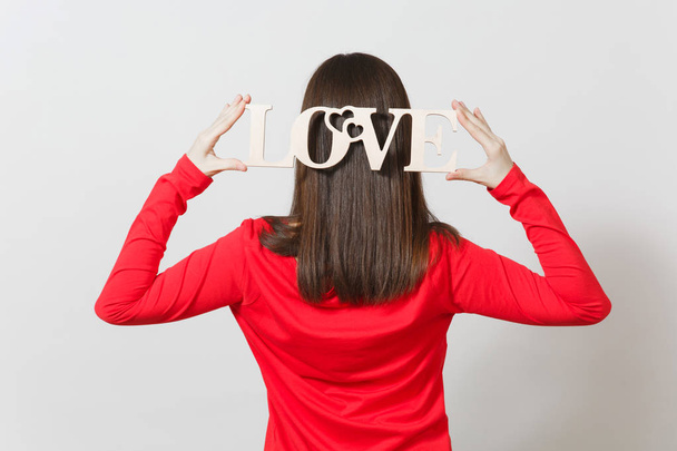 Mladá žena v červené ležérní oblečení cesty zpět do fotoaparátu, drží dřevěné slovo láska nad hlavou na bílém pozadí. Kopírovat prostor pro reklamu. Svatého Valentýna nebo mezinárodní žen s Day koncept - Fotografie, Obrázek