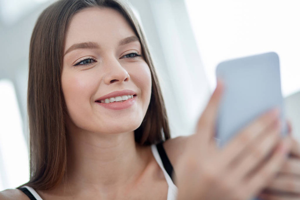 Joyful long-haired young woman using her phone - Zdjęcie, obraz