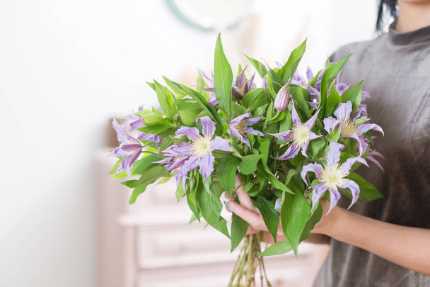 schöner luxuriöser Strauß fliederfarbener Clematis-Blüten in Frauenhand. die Arbeit der Floristin in einem Blumenladen. - Foto, Bild