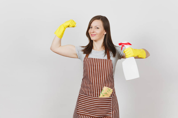 Housewife in yellow gloves, apron, cleaning rag in pocket isolated on white background. Stronge woman showing biceps muscles, holding bottle with cleaner liquid for washing dishes, sponge. Copy space. - Foto, Bild