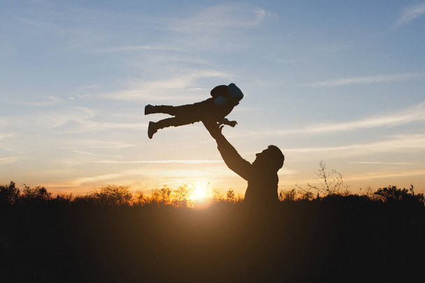 Silhouette of man high toss up little cute child baby boy on nature, sunset horizon background. Father throw up fun little kid son outdoors. Family day 15 of may, love, parents, children concept. - Foto, Imagem
