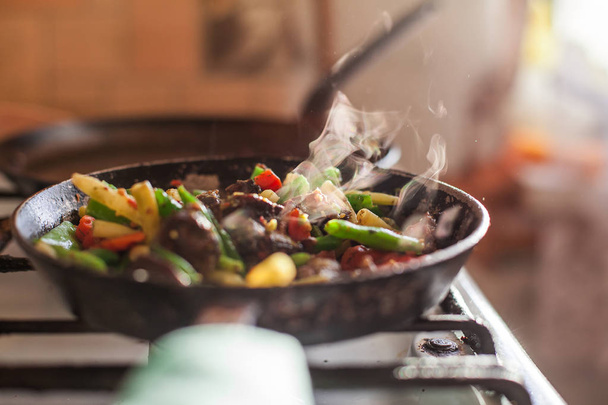 Carne roja y verduras coloridas cocinando en una sartén sucia vieja, vapor que sube en una luz del sol brillante
. - Foto, imagen