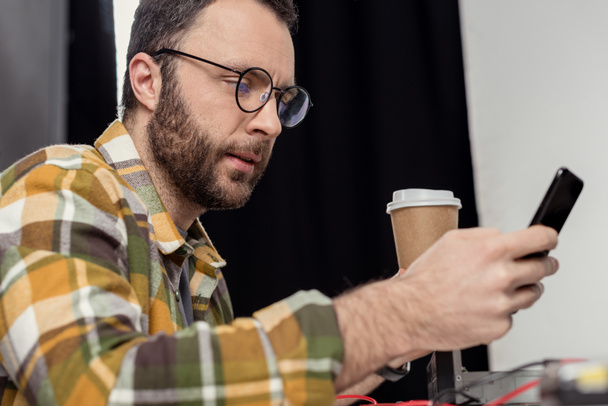 man in eyeglasses with coffee to go using smartphone - Фото, изображение