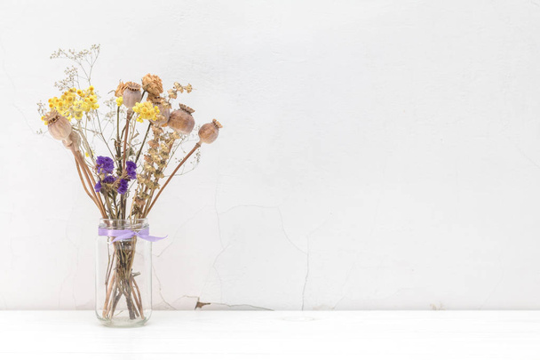 Dried flowers and poppy heads in a glass jar on white cracked wa - Fotó, kép