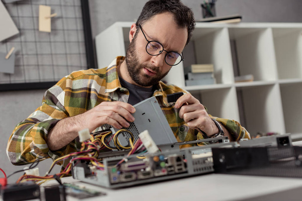 Reparaturhelfer sitzt gegen Tisch und repariert PC  - Foto, Bild