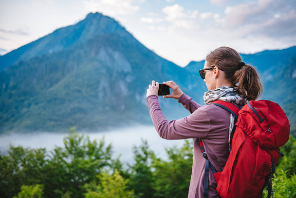 Woman with red backpack hiking on the mountain and taking picture with  smart phone - Foto, Imagen