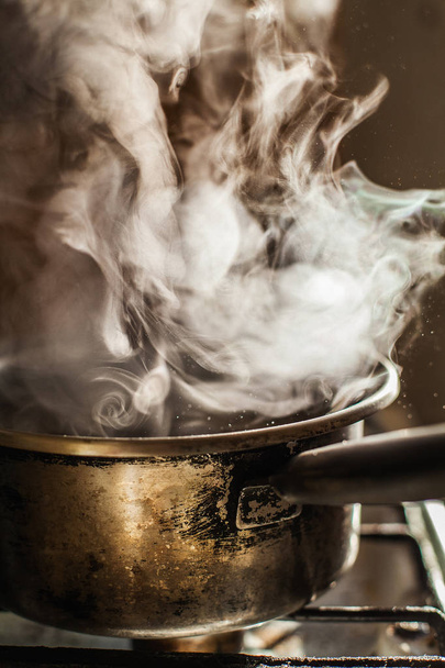 Steam rising beautifully from water boiling in an old dirty stainless steel cookware - Photo, Image