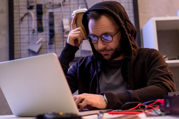 ο άνθρωπος σε hoodie χρησιμοποιούν φορητό υπολογιστή στο τραπέζι - Φωτογραφία, εικόνα