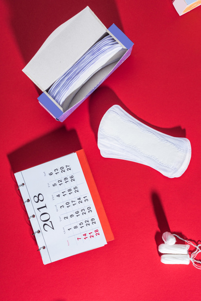 bovenaanzicht van tampons, dagelijkse voeringen en agenda op rood - Foto, afbeelding