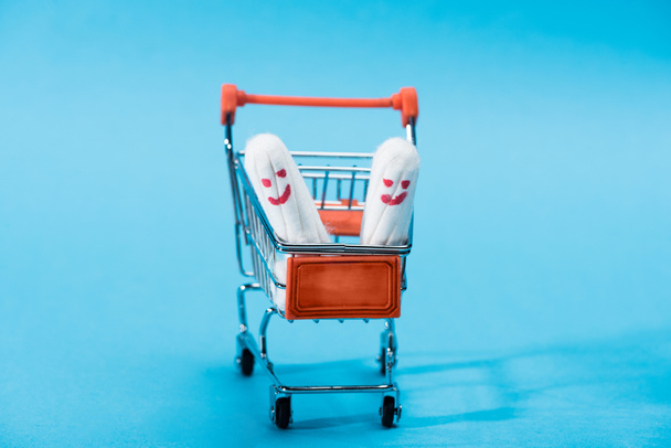 two menstrual tampons with happy smileys in small shopping cart on blue - Fotografie, Obrázek