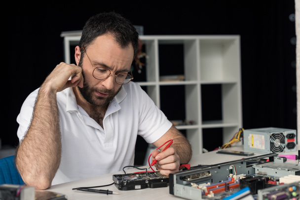 repairman with hand on cheek using multimeter while testing hard disk drive   - Photo, Image
