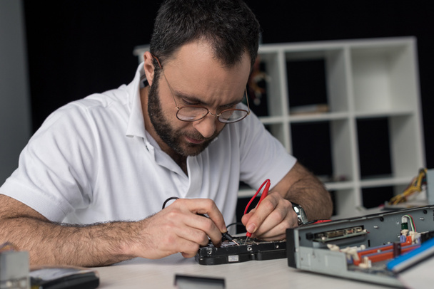 ремонтник с помощью мультиметра во время тестирования жесткого диска
 - Фото, изображение