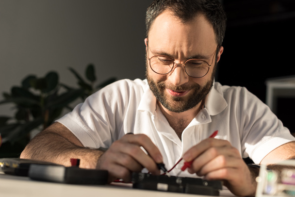 hombre sonriente usando multímetro mientras que fija la PC
 - Foto, Imagen