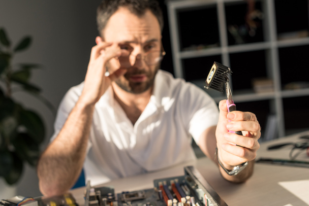 hombre sosteniendo parte del ordenador en la mano con pinzas
 - Foto, Imagen