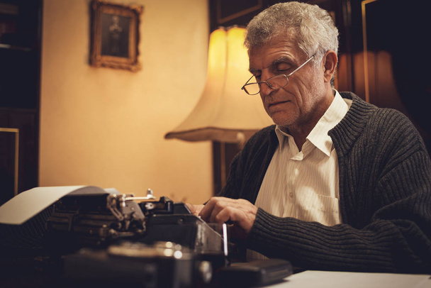 Retro Senior uomo scrittore con occhiali di scrittura sulla macchina da scrivere obsoleta
. - Foto, immagini