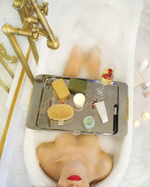 Привлекательная девушка расслабляется в ванной с подносом косметики
  - Фото, изображение