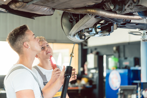 熟練した自動車整備士、現代の自動車修理店で一緒に作業しながらリフト車のショックアブソーバーの交換の側面図 - 写真・画像