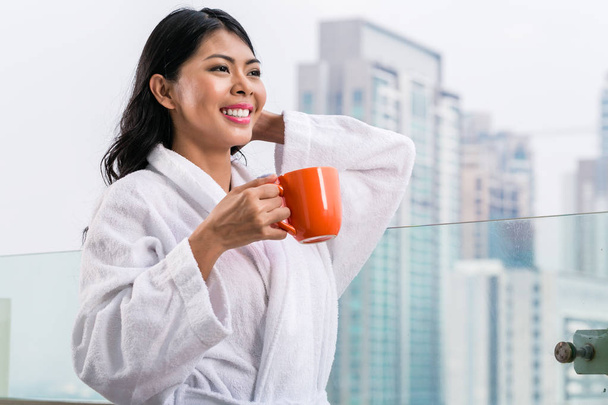 Asian woman drinking coffee in morning in front of city skyline  - 写真・画像