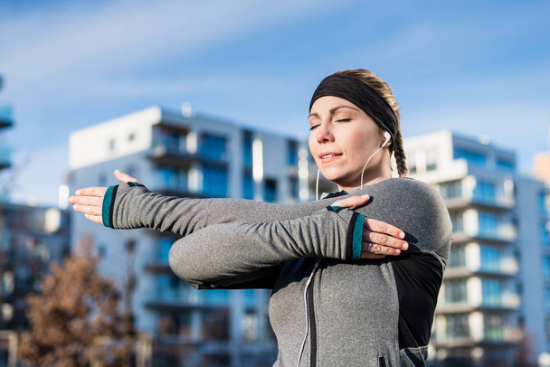 Portrait d'une jeune femme déterminée étirant son bras gauche pendant la routine d'échauffement avant l'entraînement en plein air pendant la journée ensoleillée
 - Photo, image