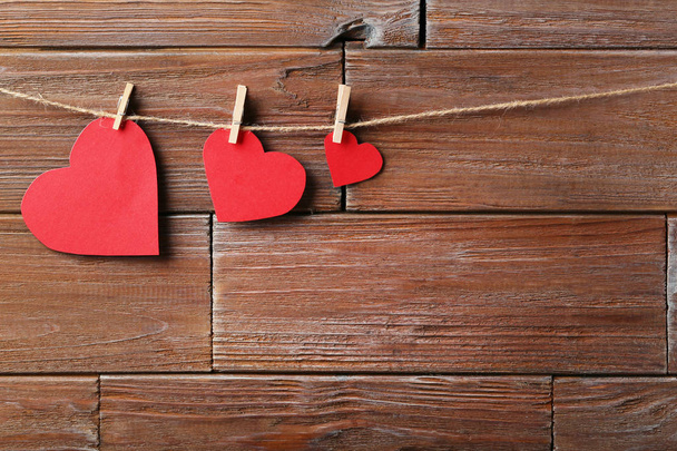 Red paper hearts hanging on wooden background - 写真・画像