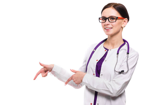 Молода жінка-лікар зі стетоскопом, що вказує пальцями
 - Фото, зображення