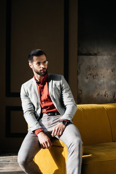 модный элегантный мужчина в очках и костюме сидит на диване
  - Фото, изображение