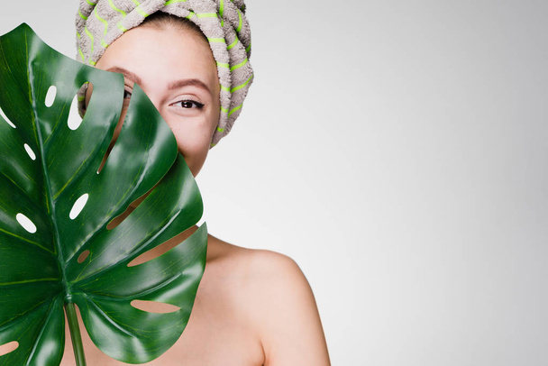 cute young girl enjoying spa treatments, holding a green leaf, wearing a towel on her head - Zdjęcie, obraz