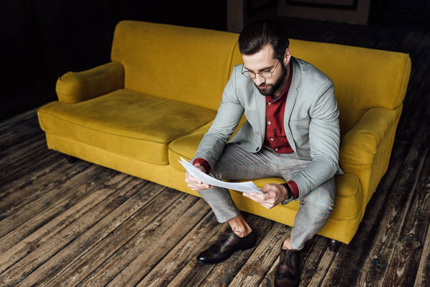 tyylikäs mies trendikäs harmaa puku lukeminen sanomalehti ja istuu sohvalla
  - Valokuva, kuva