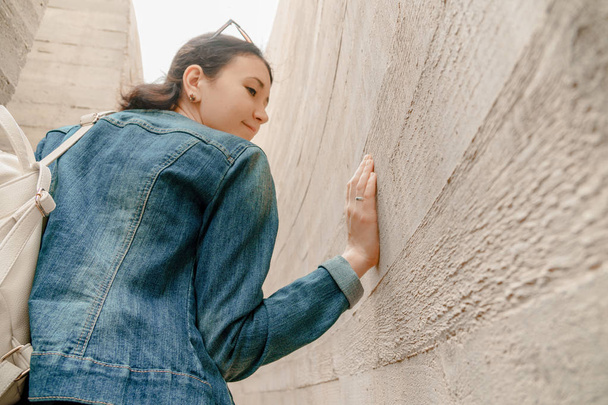 Atrakcyjna młoda kobieta stoi pomiędzy ścian betonowych. Kaukaski dziewczyny w dżinsy casual i sukienka spogląda wstecz - Zdjęcie, obraz
