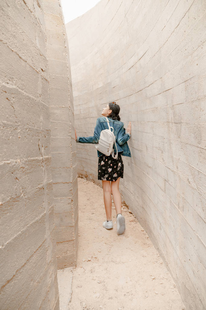 Atractiva joven mujer se encuentra entre muros de hormigón. Caucásico chica en casual jeans mira hacia arriba
. - Foto, Imagen
