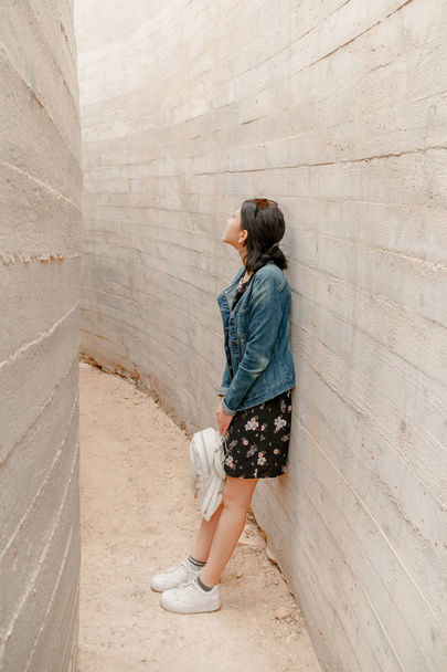 Aantrekkelijke jonge vrouw staat tussen de betonnen muren. Kaukasische meisje in casual jeans worden opgezocht. - Foto, afbeelding
