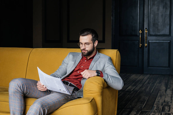 stylish handsome man reading newspaper and sitting on couch - Φωτογραφία, εικόνα