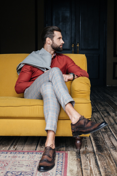 fashionable man in suit and brogue shoes sitting on yellow sofa in loft interior - Foto, Imagen