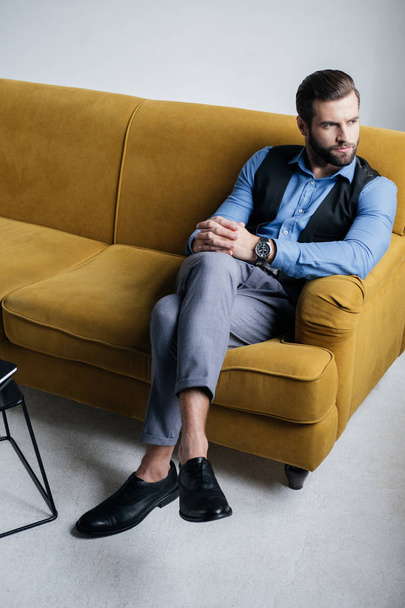 stylish man sitting on yellow sofa - Фото, зображення