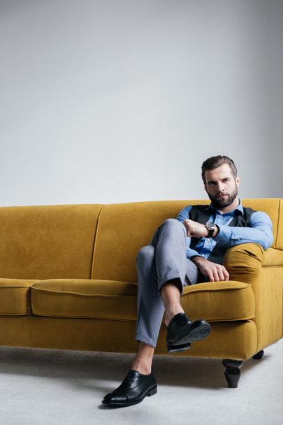 stylish elegant man sitting on yellow sofa - Photo, Image